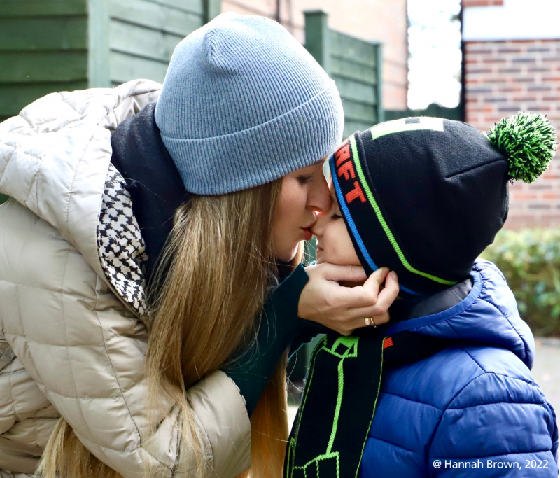 A woman kisses a boy. They're both wearing warm clothes