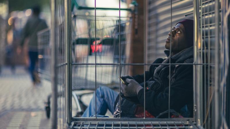 Man sitting on the floor next to shop shutters. 